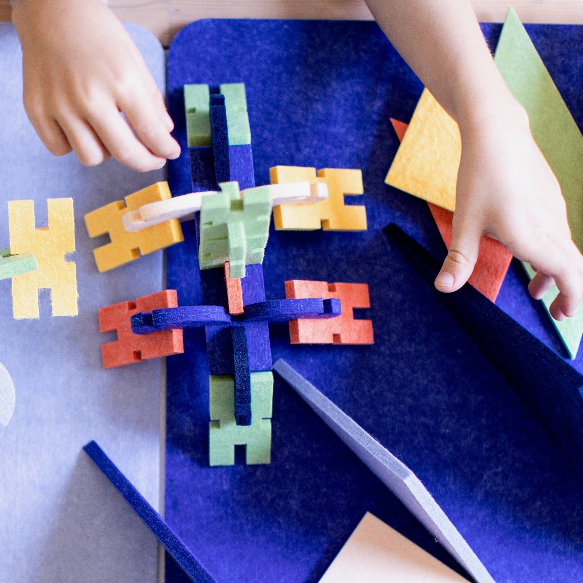 a child's hands build and rearrange colorful interlocking block pieces arranged in the shape of a giant spider near a mountain range created from oversize triangle pieces.